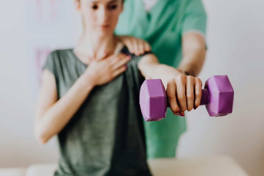 Physiotherapist helping young woman with shoulder exercises.