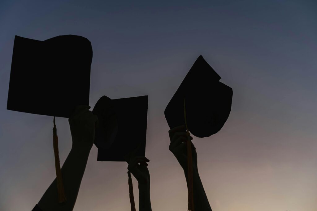 Silhouetted graduates celebrating at dusk with caps held high, symbolizing success and new beginnings.